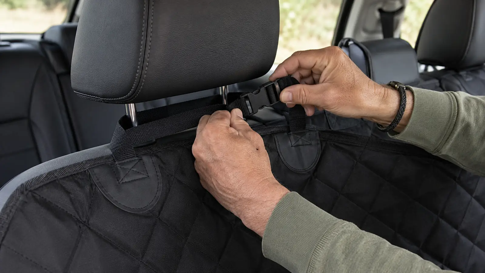 Hands routing a hammock style car seat cover strap around a headrest post during installation